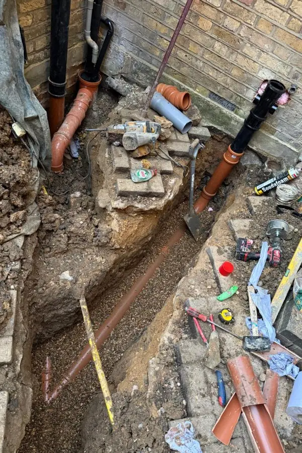 Open excavation with new orange drainage pipe being installed